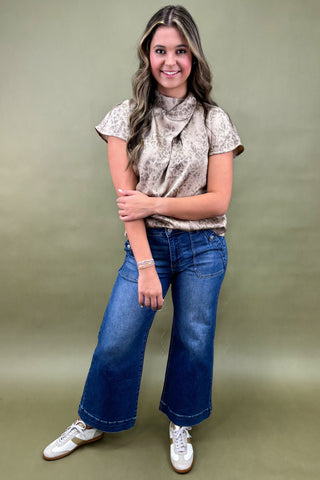 Woman wearing a patterned top and blue jeans against a green background