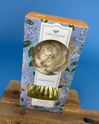 Greenleaf Est. 2015 Laurel Grove citrus oil in a decorative floral box with a clear window showing the pale yellow oil and a gold cap, set on a wooden block against a blue background.
