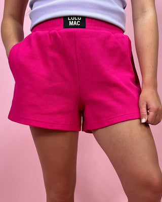 Person wearing bright pink shorts with a visible brand label on a pink background