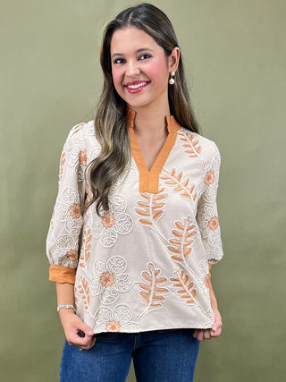 Woman wearing a white blouse with orange floral embroidery against a green background