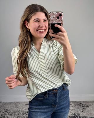 Woman taking a mirror selfie wearing a striped shirt and jeans against a plain background