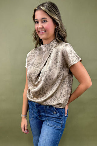 Woman wearing a patterned blouse and blue jeans against a green background