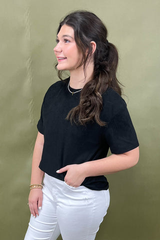 Woman wearing a black t-shirt and white pants against a green background