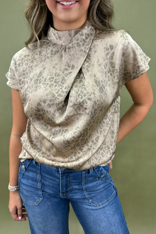 Woman wearing a patterned blouse and blue jeans against a green background