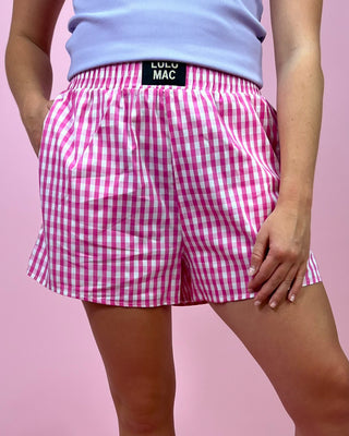 Person wearing pink gingham shorts with a visible brand label on a pink background