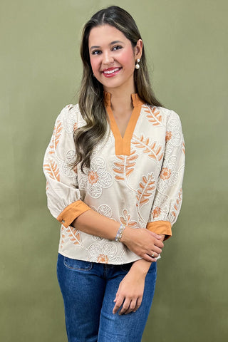 Woman wearing a white blouse with orange accents and blue jeans against a green background