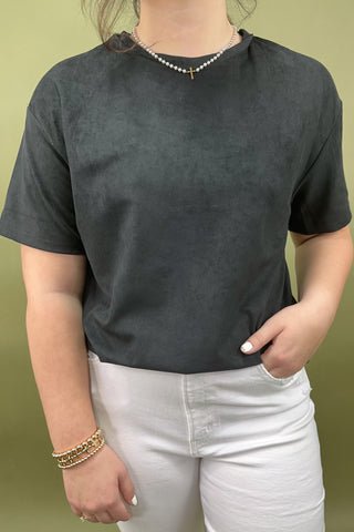 Person wearing a dark gray t-shirt and white pants against a green background