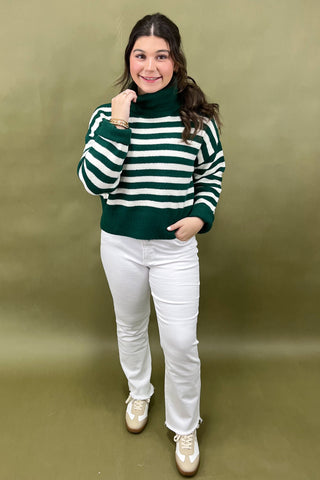 Woman wearing a green and white striped sweater with white pants against a green background