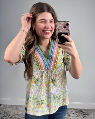 Woman taking a mirror selfie wearing a colorful floral blouse with a gray background