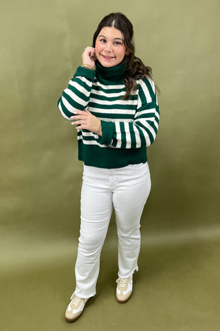 Person wearing a green and white striped sweater with white pants on a green background