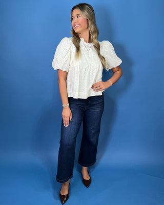 Ivory eyelet blouse with lace detailing, a ruffle neckline, and statement puff sleeves.