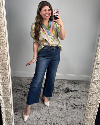 Woman taking a mirror selfie wearing a floral blouse and blue jeans.