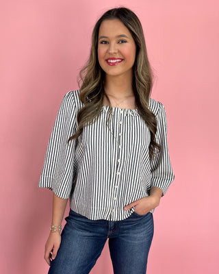 Woman wearing a black and white striped blouse with blue jeans against a pink background