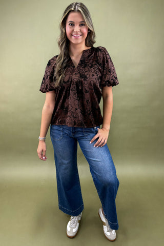 Woman wearing a brown patterned top and blue jeans on a green background