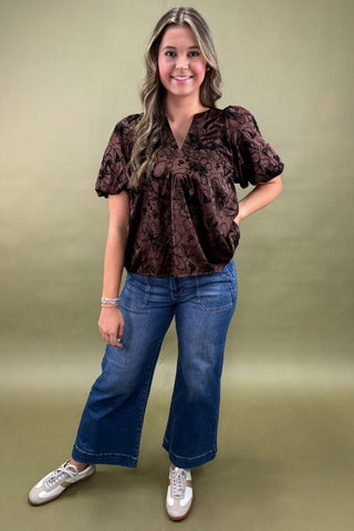 Woman wearing a brown patterned blouse and blue jeans on a green background