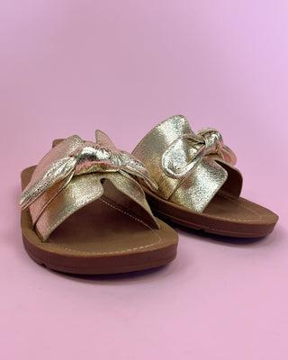 Gold sandals with a bow on a pink background