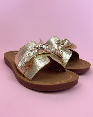 Gold sandals with a bow on a pink background