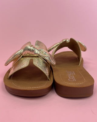 Gold sandals with a bow design on a pink background