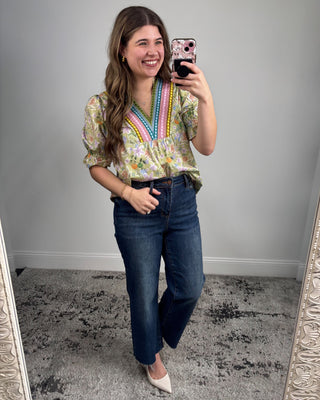 Woman taking a mirror selfie wearing a colorful blouse and blue jeans.