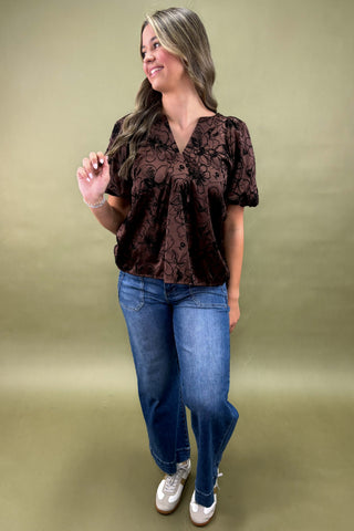 Woman wearing a brown blouse and blue jeans against a green background