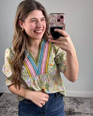 Woman taking a mirror selfie wearing a colorful blouse with bead details.
