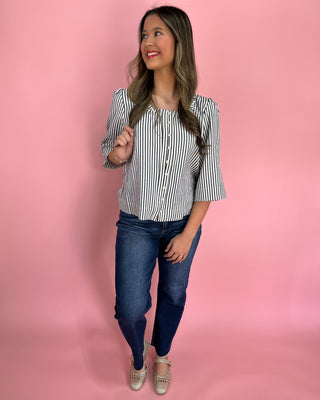 Woman wearing a striped shirt and jeans against a pink background