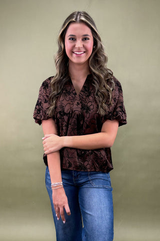 Woman wearing a brown floral blouse and blue jeans against a green background