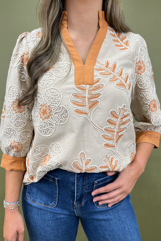 Woman wearing a floral blouse with orange accents and blue jeans against a green background