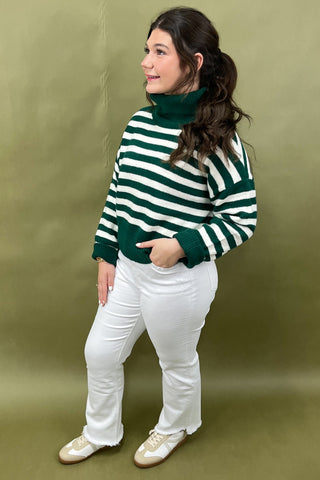 Person wearing a green and white striped sweater with a green turtleneck underneath, standing against a green background.