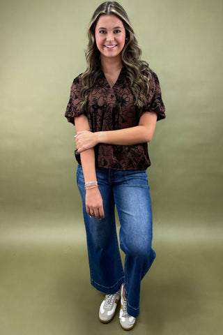 Woman wearing a patterned shirt and jeans on a green background