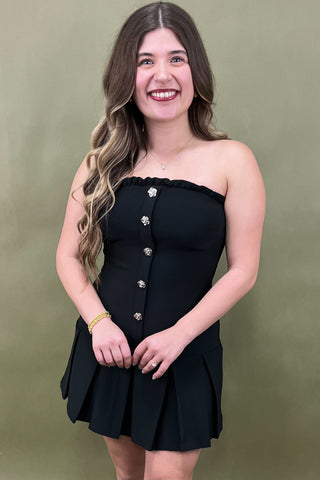 Woman wearing a black strapless dress with silver buttons against a green background