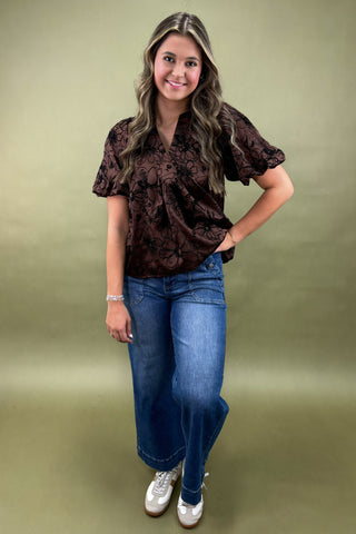 Woman wearing a brown patterned blouse and blue jeans on a green background