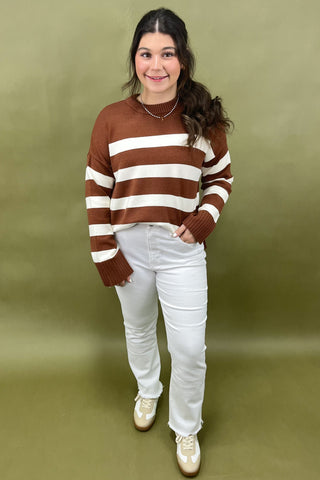 Person wearing a brown and white striped sweater with white pants against a green background