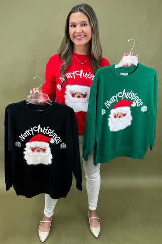 Woman holding three Christmas-themed sweaters with 'Merry Christmas' and Santa Claus designs on a green background.