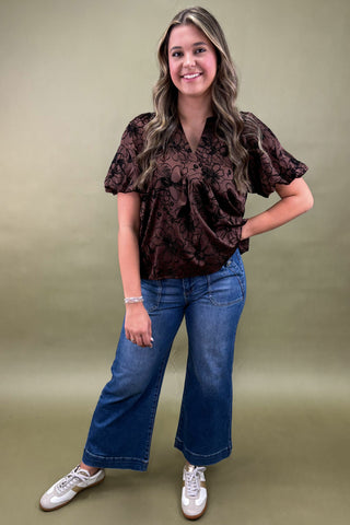 Woman wearing a brown patterned blouse and blue jeans on a green background