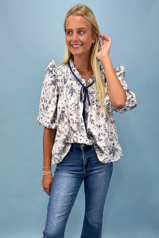 Woman wearing a floral blouse and blue jeans against a light blue background