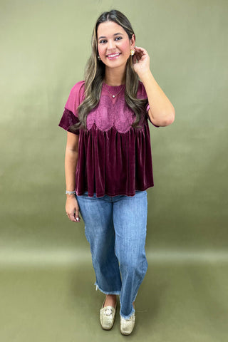 Woman wearing a burgundy top with lace details and blue jeans on a green background