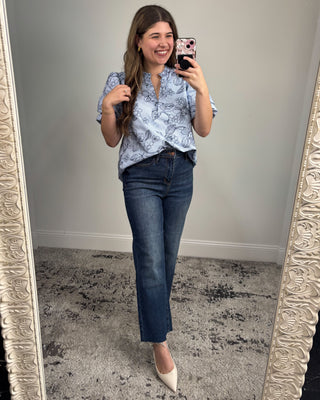 Woman taking a mirror selfie wearing a blue patterned blouse and jeans.