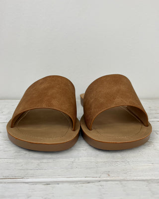 Pair of brown sandals on a light wooden floor with a white background