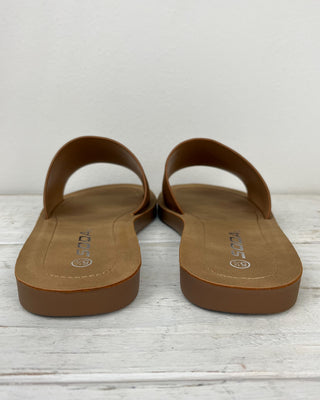 Pair of brown sandals on a light wooden floor with a white background