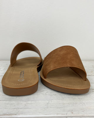 Pair of brown sandals on a light wooden surface with a white background
