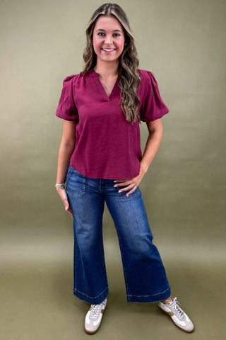 Woman wearing a maroon top and blue jeans against a green background