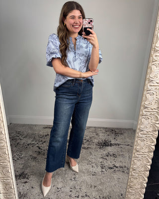 Woman taking a mirror selfie wearing a blue patterned blouse and jeans.