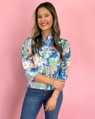 Woman wearing a floral blouse and jeans against a pink background