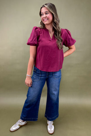 Woman wearing a maroon top and blue jeans against a green background