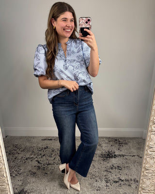 Woman taking a mirror selfie wearing a floral blouse and jeans.