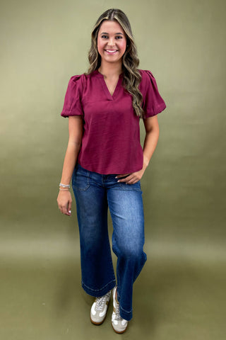 Woman wearing a maroon top and blue jeans against a green background
