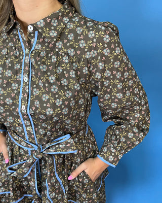 A woman modeling a brown long-sleeve mini dress with a white floral pattern and light blue trim