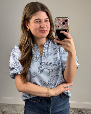 Woman taking a mirror selfie wearing a floral blouse and jeans.