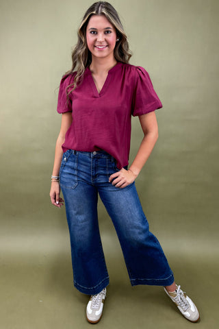 Woman wearing a maroon top and blue jeans against a green background